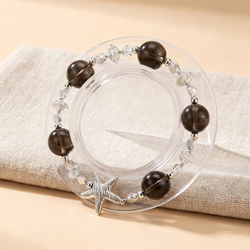 Clear bracelet with brown beads and a starfish charm on a beige fabric background