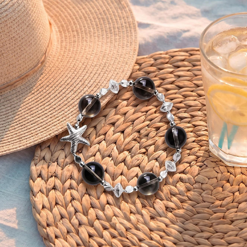 Bracelet with starfish and black bead design on a woven mat with a hat and glass of lemonade.