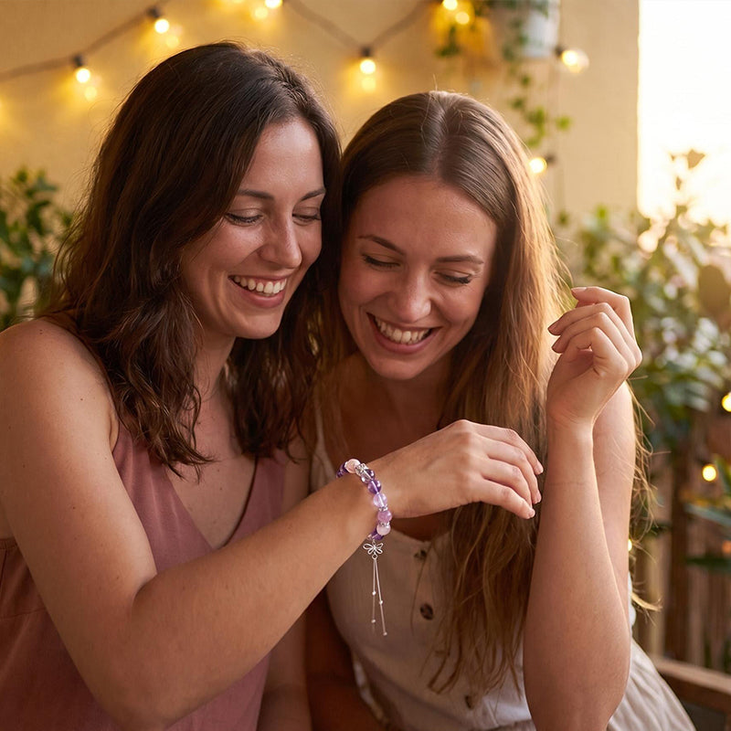 Two women smiling and looking at a bracelet with a decorative charm.